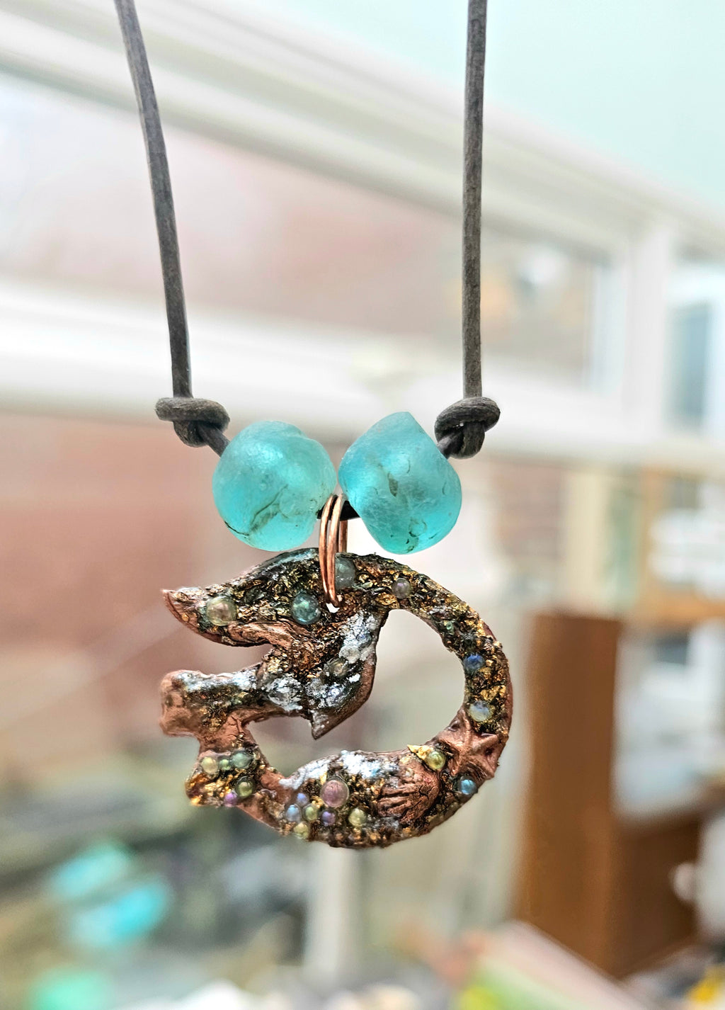 Necklace with a copper mermaid pendant and turquoise beads against a blurred indoor background