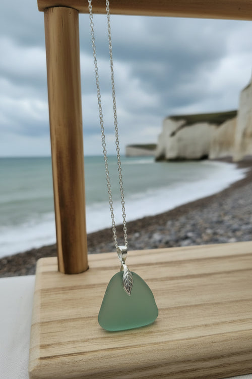Green sea glass pendant on a silver chain displayed on a wooden stand.