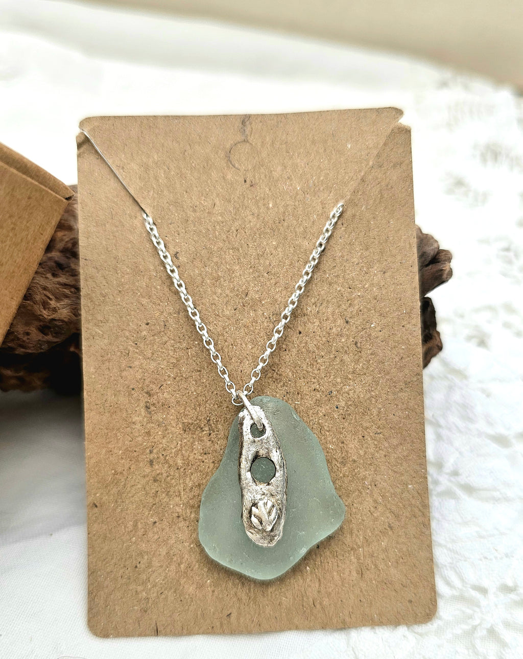 A light blue authentic hand-picked sea glass pendant with fine silver charm and chain highlighted on recycled card.