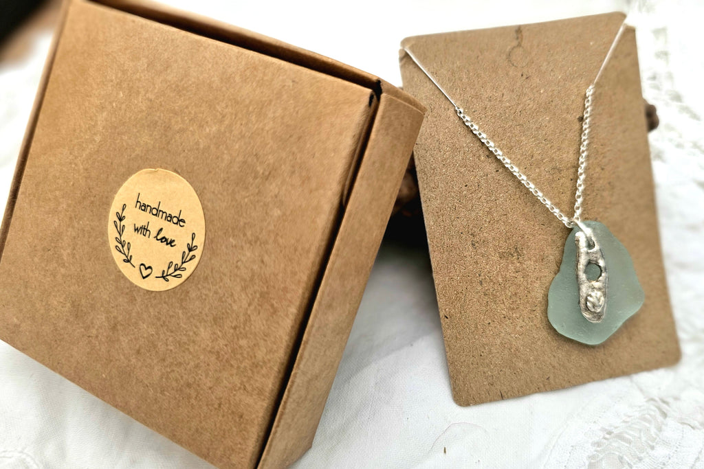 A light blue authentic hand-picked sea glass pendant with fine silver charm and chain with recycled packaging.