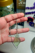A small sterling silver branching bail and stainless steel chain holding a sea glass pendant draped over a hand with a blurred jewellery studio background